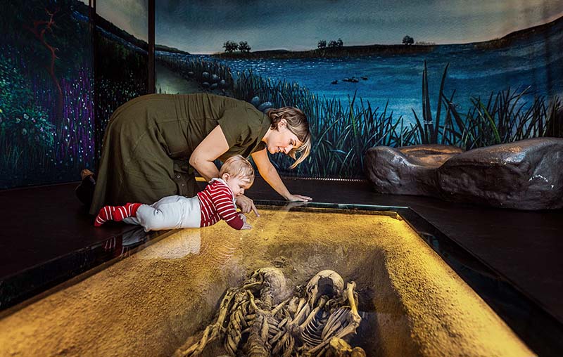 Vy från Öga mot Öga med en kvinna och en bebis tittar på två skelett.