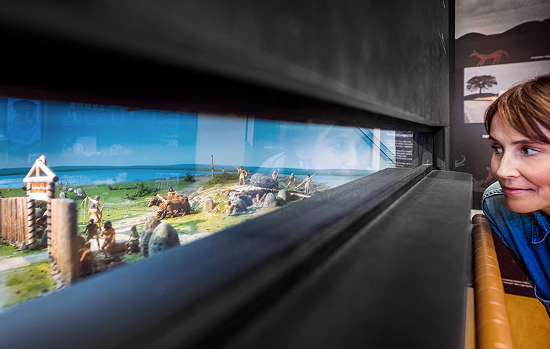 Vy från Öga mot Öga med en kvinna som tittar på en panoramamiljö från bondestenåldern.