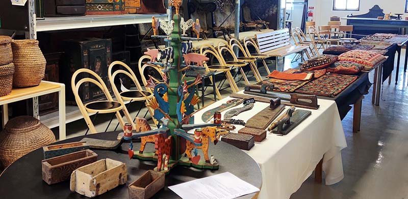 Ett långt bord med träföremål och textilföremål står uppställt framför en rad med stolar.