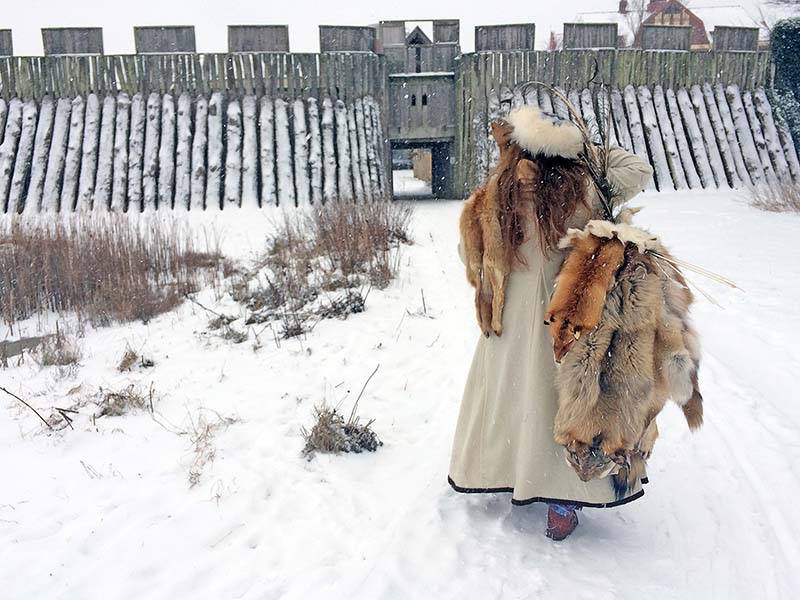 Snötäckt vikingaborg. En vikingaklädd kvinna går mot borgen.