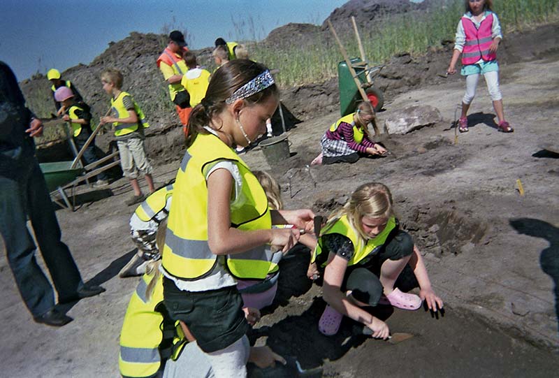 Elever gräver i jorden på en arkeologisk utgrävning.