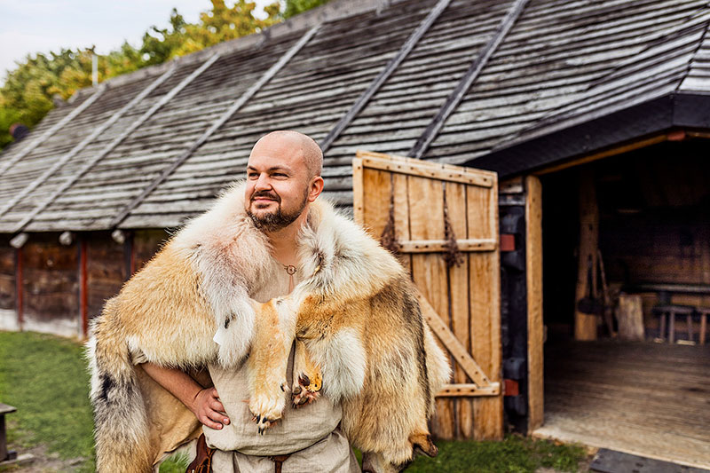 Viking klädd i päls välkomnar framför vikingahuset.