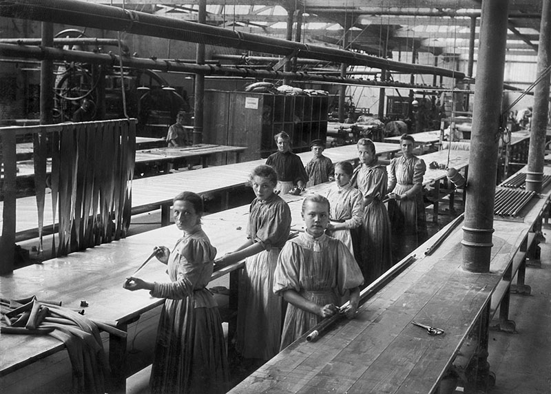 Äldre foto från gummifabriken. Sju kvinnor och en pojke syns arbeta närmast i bilden.