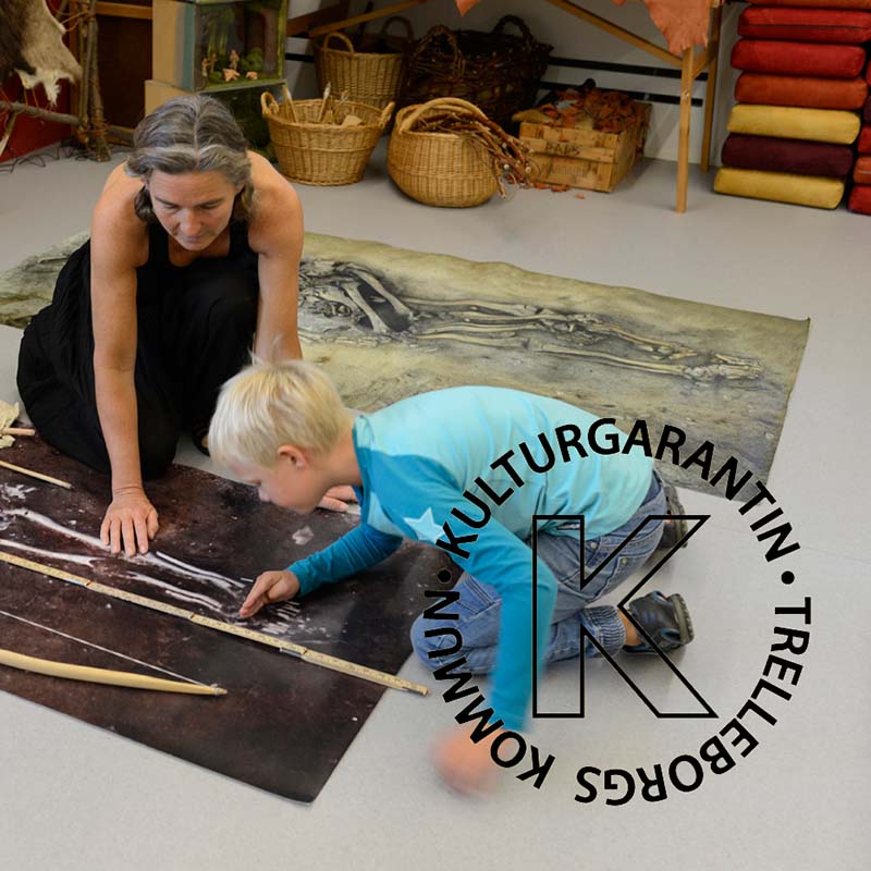 Pojke mäter ett barnskelett med tumstock på ett stort foto på golvet tillsammans med pedagog.