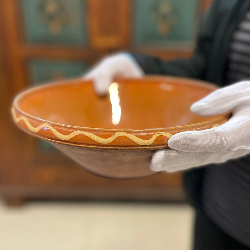 Närbild av två händer med vita handskar som håller i en skål av lera.