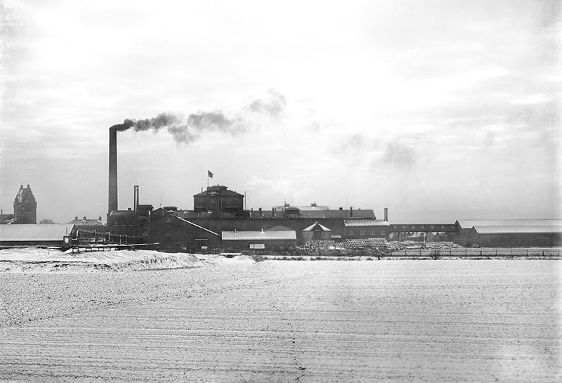 Äldre svart och vit bild med vy över sockerbruket från norr, med Trelleborgs kyrka till vänster.