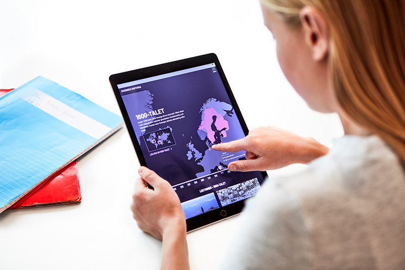 A girl sitting with a tablet, accessing sverigeshistoria.se.