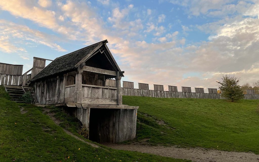 Vy över den återskapade vikingaborgen från dess insida med vacker blå himmel, porthus, borgvall och bröstvärn.