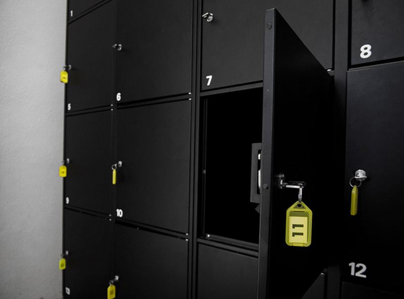 Black storage lockers against a white wall. Yellow keys with numbers on the locks. White numbers on the locker doors.