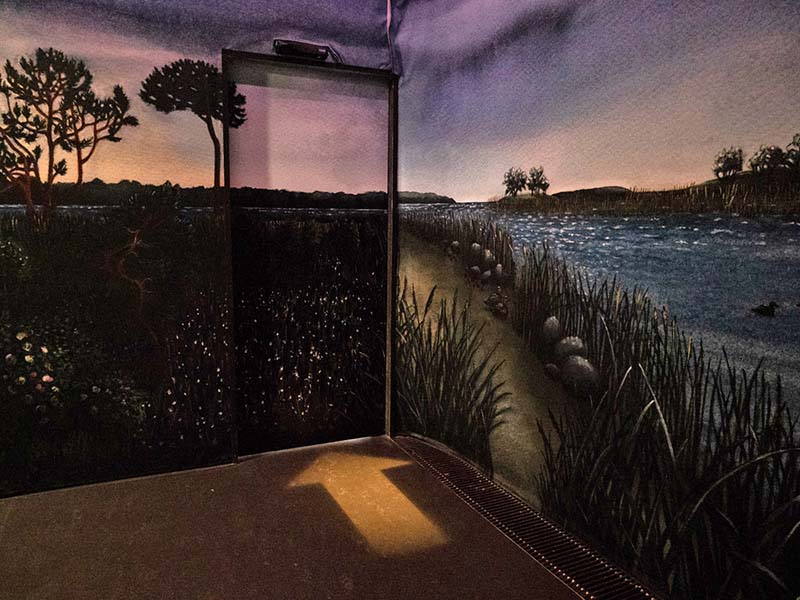 The next room is dark with walls painted with nature motifs. There is a door with the same painting. There is an arrow on the floor pointing towards the door.