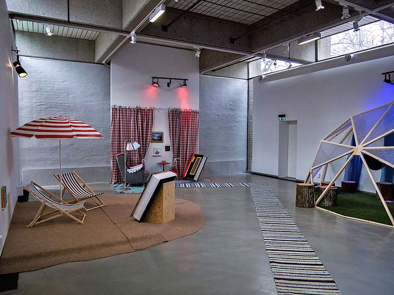 Bright open room with white walls and a gray floor. There are carpets and chairs on the floor.