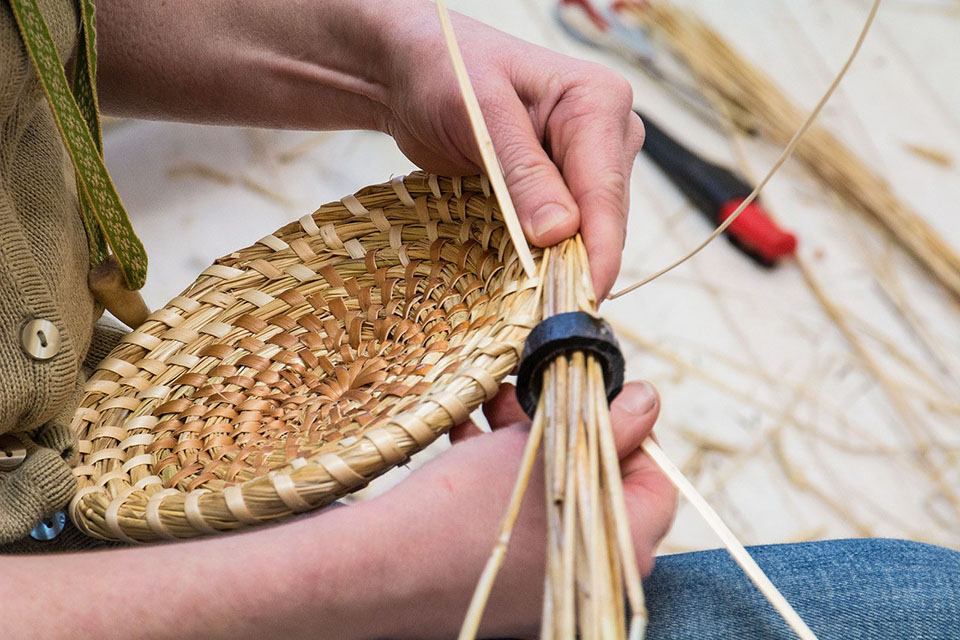 En person gör en korg med halmöbteknik.