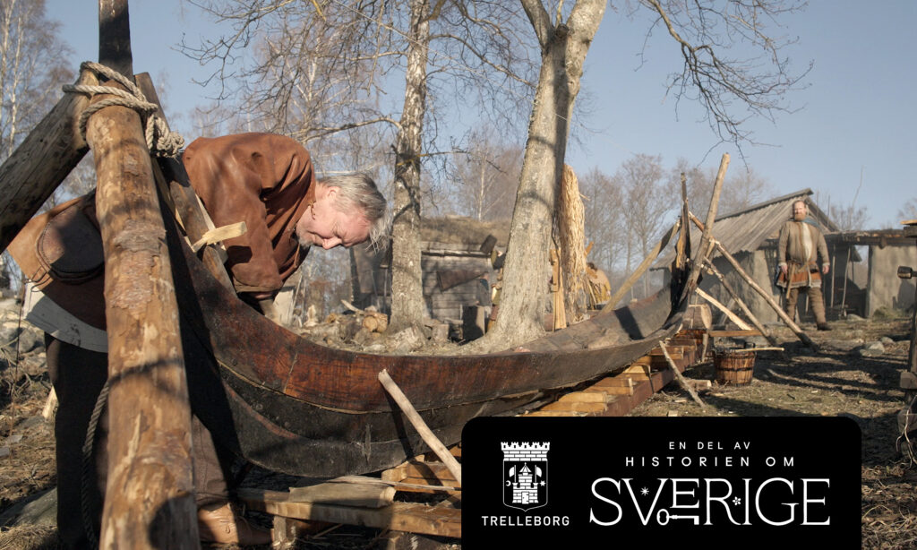 Man i kläder av skinn arbetar med en träbåt.