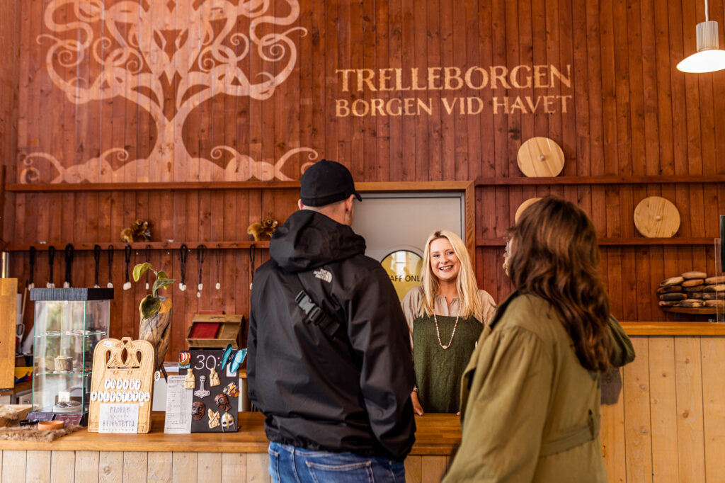 Receptionen på Vikingamuseet Trelleborgen. Två personer pratar med en kvinna i vikingakläder som står bakom disken.