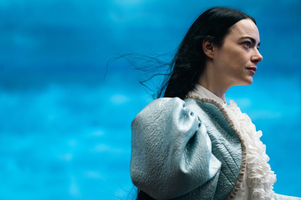 Bild från filmen Poor Things. Kvinna i blå klänning mot blå bakgrund