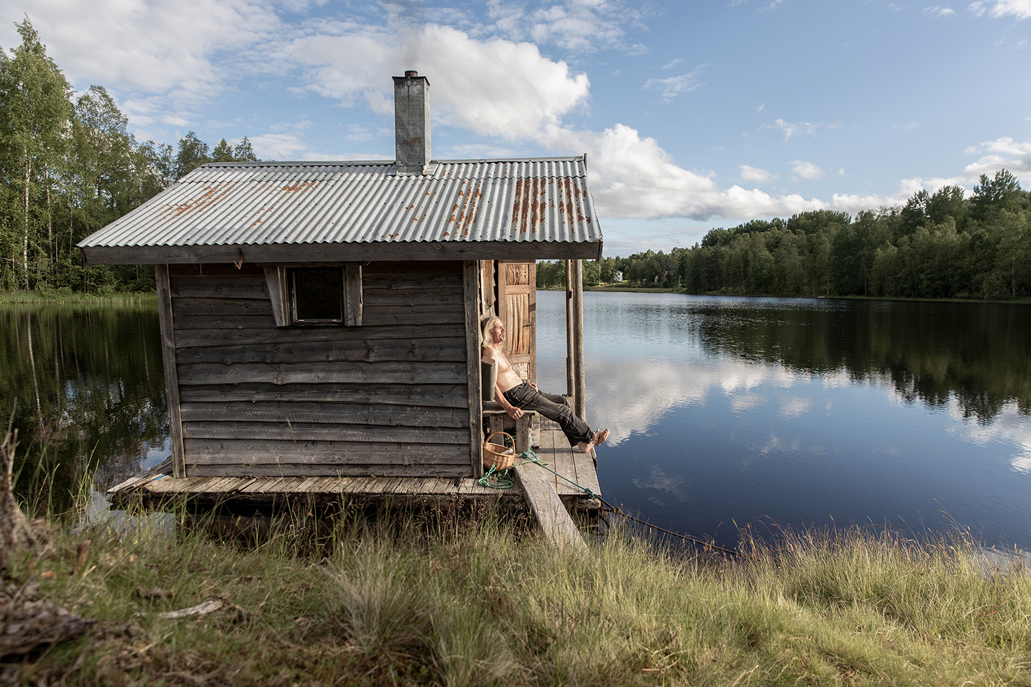 Bastu vid kanten av en sjö. En man tittar ut över sjön.