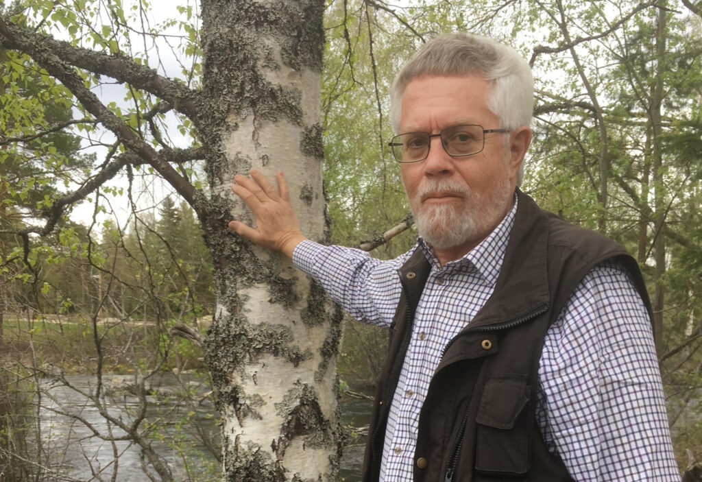 man, Lennart Rohdin, står vid en sjö med handen på en björk.