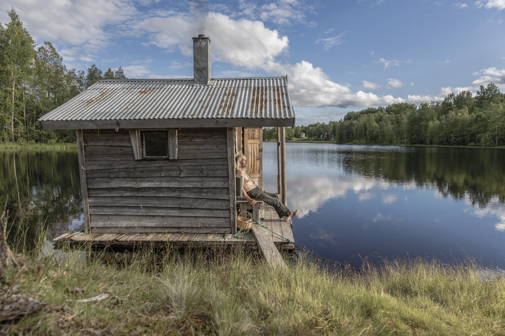 Bastu vid kanten av en sjö. En man tittar ut över sjön.