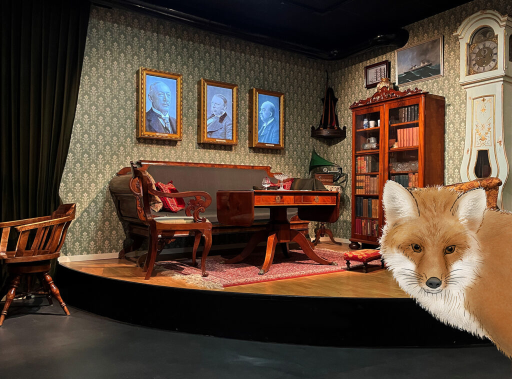 En räv tittar fram. bakom ser man ett elegant möblerat rum.