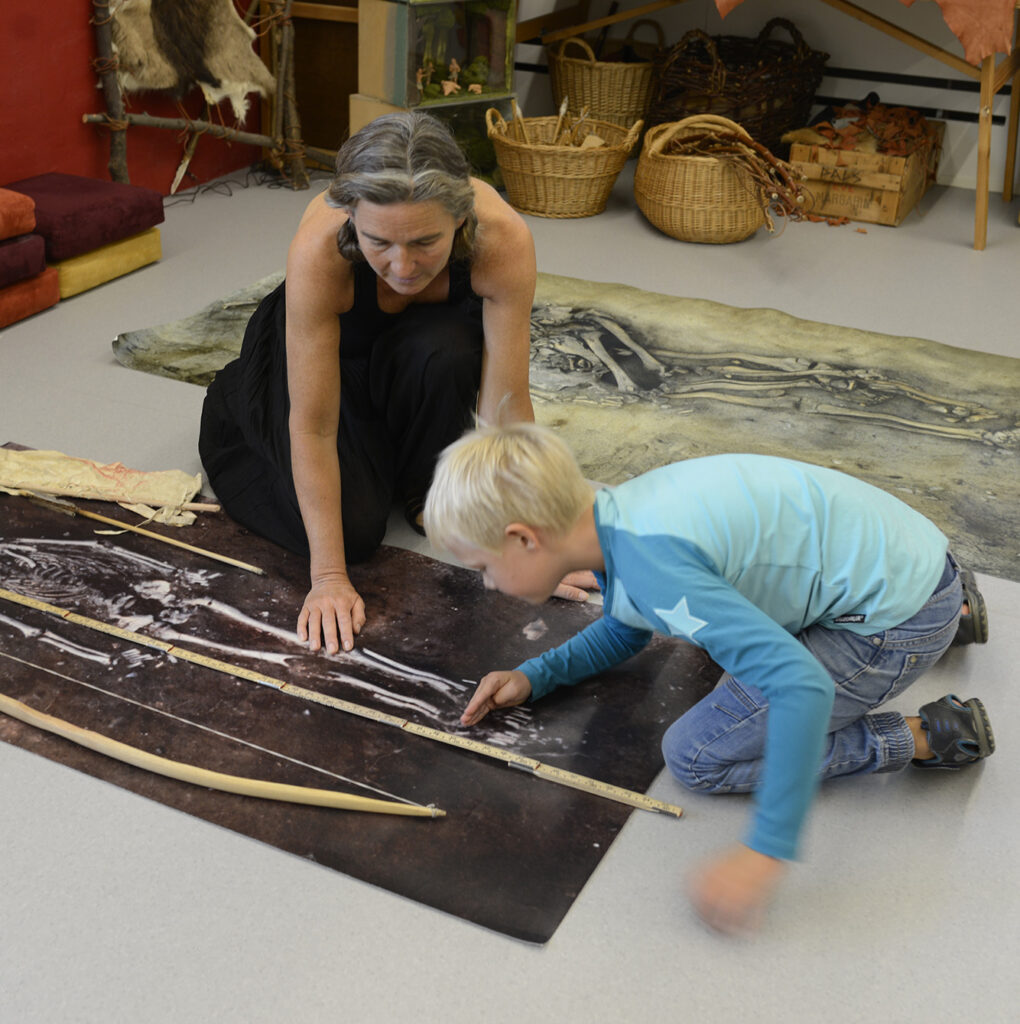 En lärare och en pojke tittar på ett stort foto av ett skelett i en grav från stenåldern.