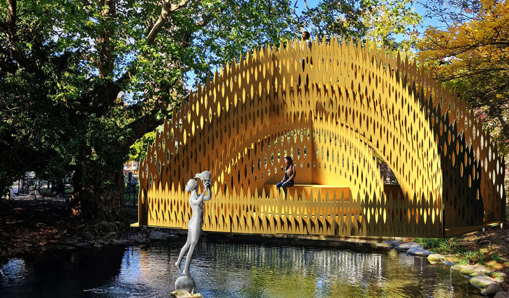 Gul halvcirkelformad bro över en liten damm. I förgrunden en bronsskulptur av en naken kvinna